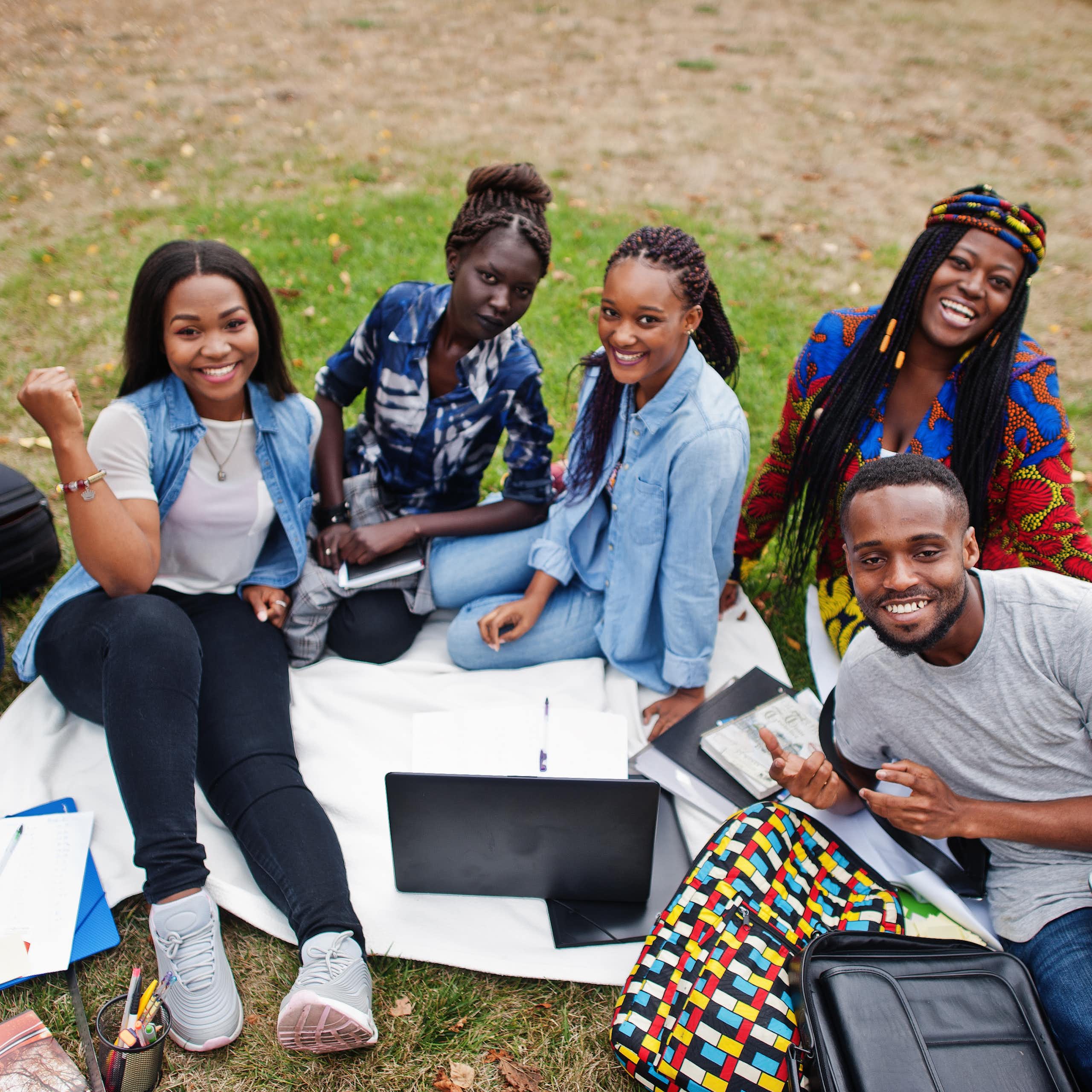 A group of Black students with laptops and knapsacks sitting outdoors.