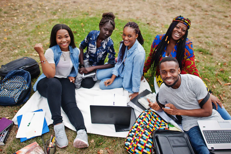 A group of Black students with laptops and knapsacks sitting outdoors.