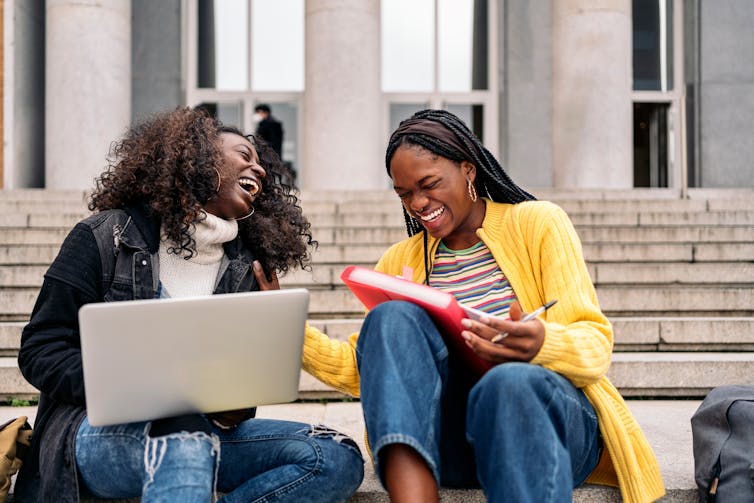 Two Black women laughing on steps.