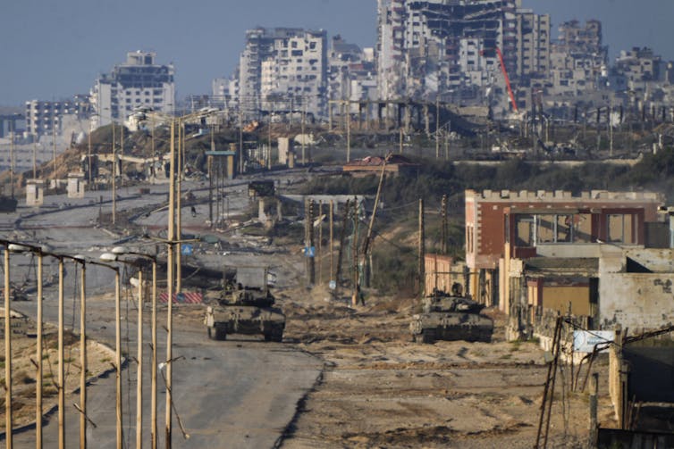 Israeli Army tanks sit in the foreground with bombed out buildings in the distance in central Gaza.
