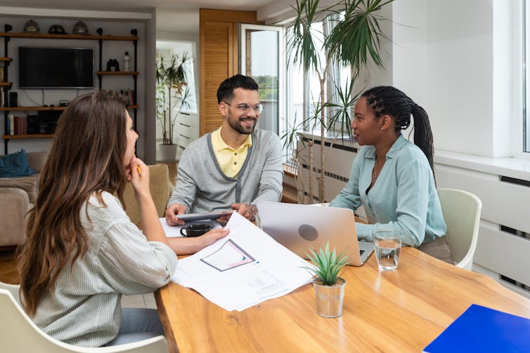 Three young adults sitting around a table having a conversation in an office space