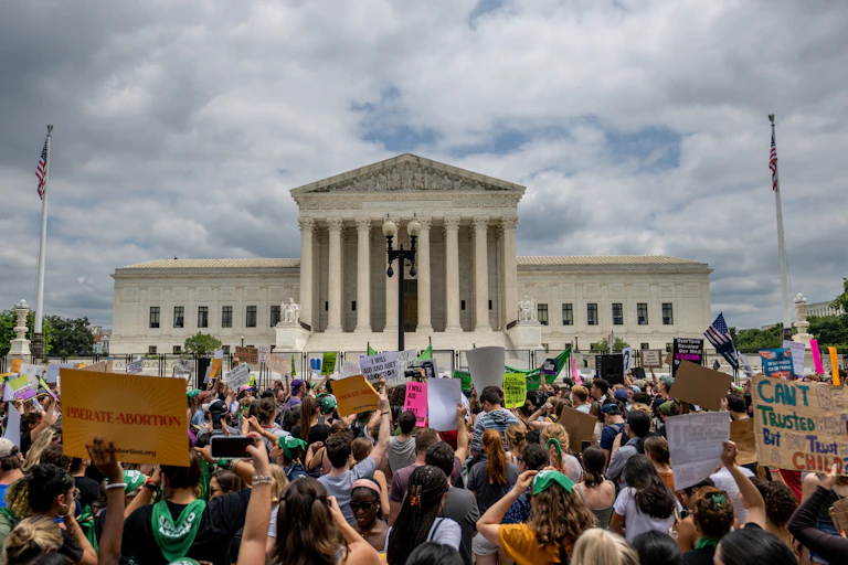 A crowd of protesters in front of a large white building with pillars in front.