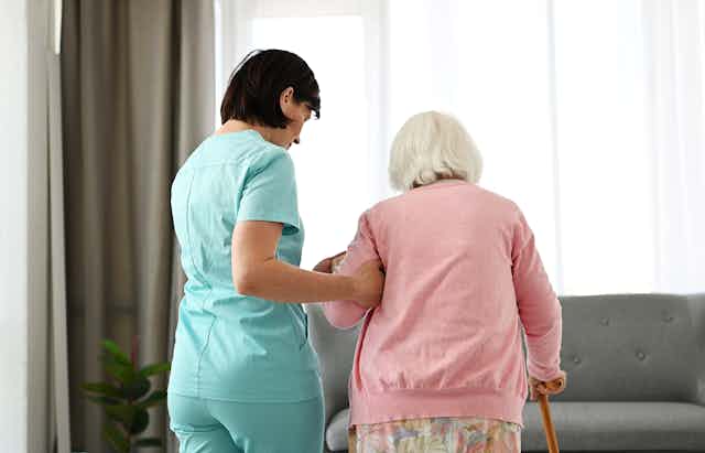 A nurse helps a senior woman move around a room.