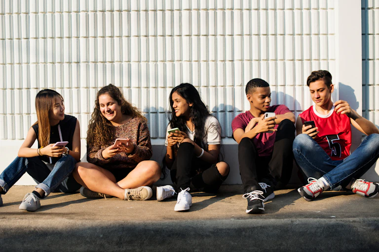 Five diverse teens sitting on the ground socialising over smartphones.