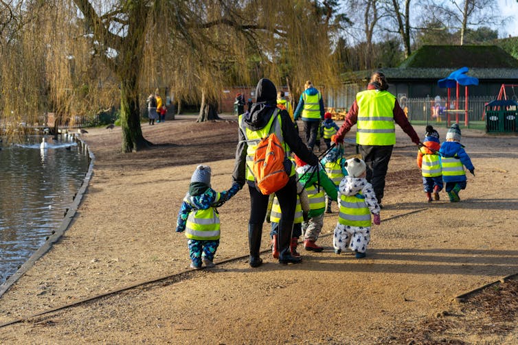 Nursery staff take small children in high-vis vests to a park.