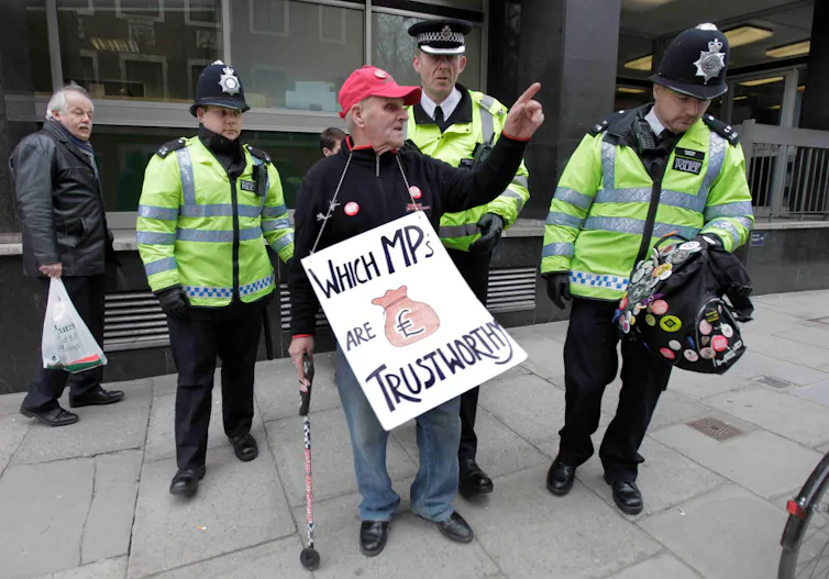 A man with a sign demonstrating against the expenses scandal being escorted by police.