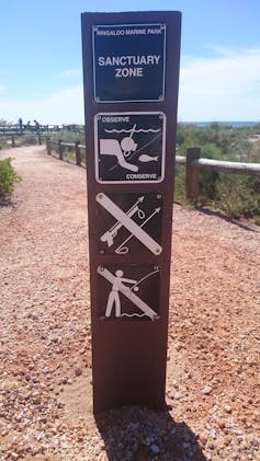 Brown sign with marine conservation logos that explain look, don't touch, gravel path and blue sky in background