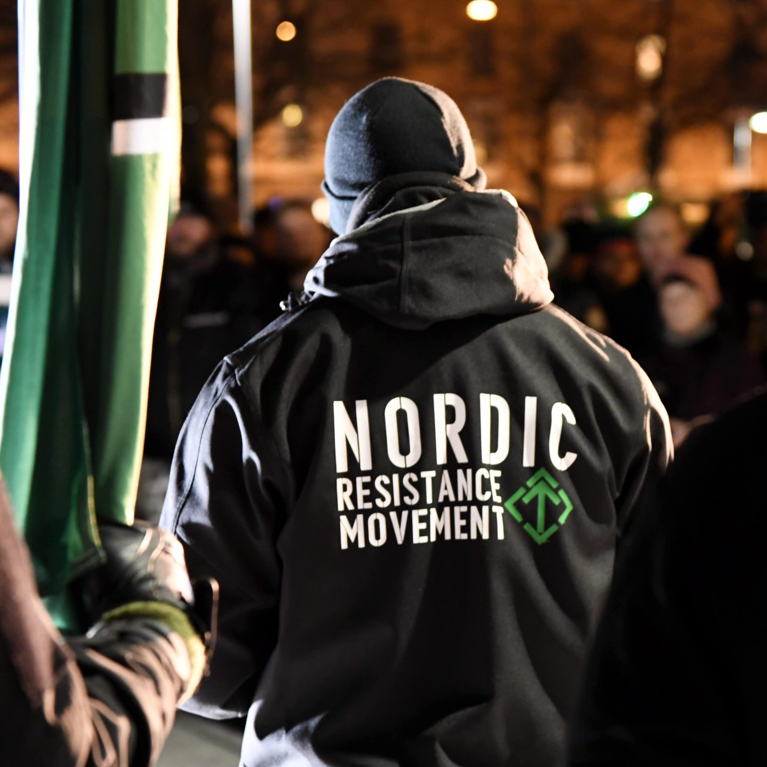 A man is seen from behind wearing a black jacket that reads "Nordic Resistance Movement."