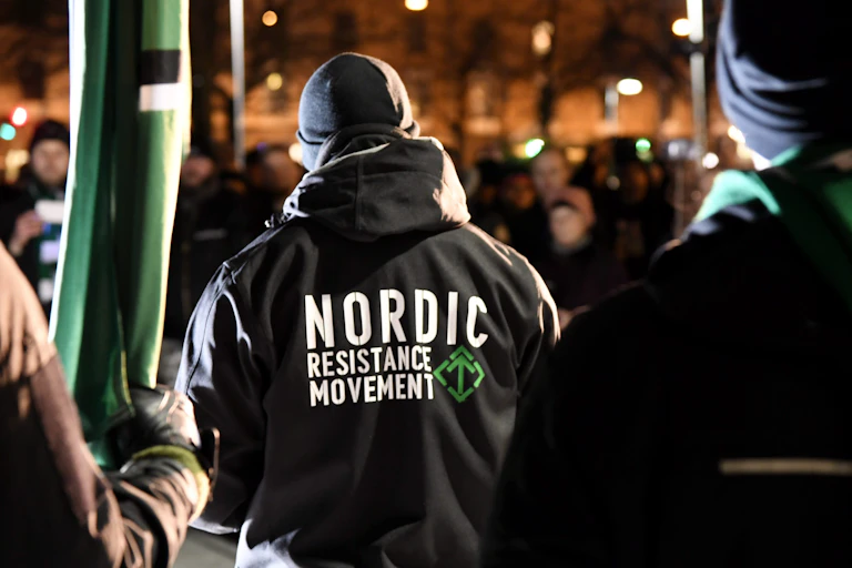 A man is seen from behind wearing a black jacket that reads "Nordic Resistance Movement."