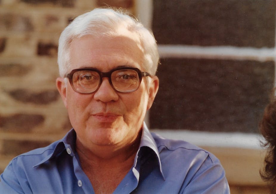 A man with grey hair and horn-rimmed glasses smiles slightly for the camera.