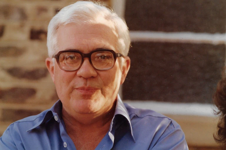 A man with grey hair and horn-rimmed glasses smiles slightly for the camera.