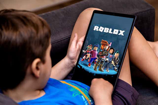 a boy holds an tablet with a screen showing animated characters and the title roblox