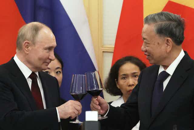 Putin and the Vietnamese president toast one another with a glass of wine in hand.