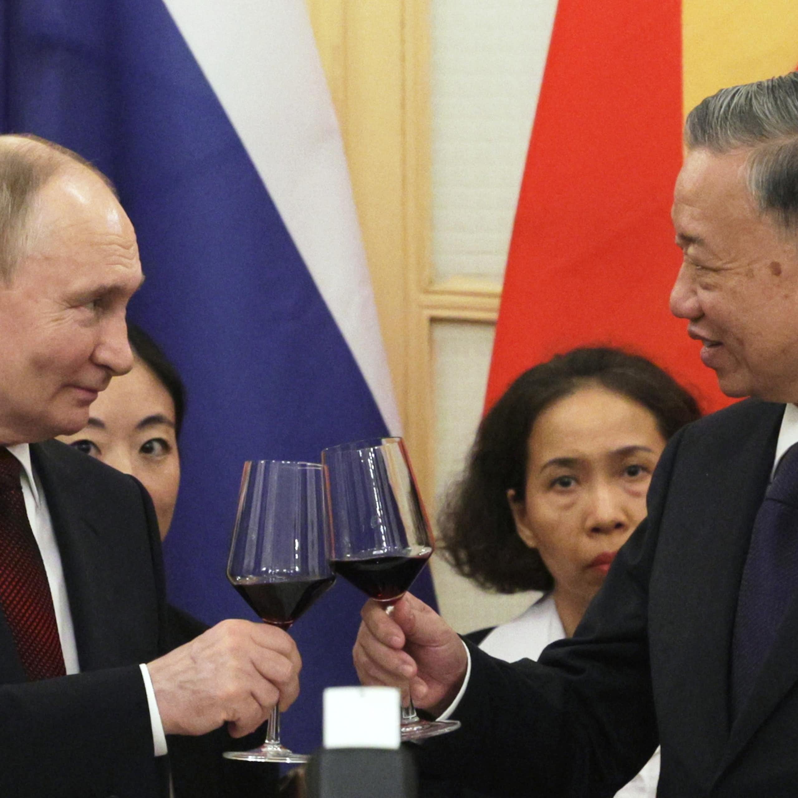 Putin and the Vietnamese president toast one another with a glass of wine in hand.