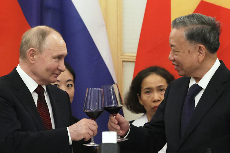 Putin and the Vietnamese president toast one another with a glass of wine in hand.