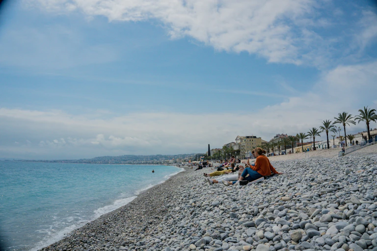 Une plage de galets, sur laquelle des personnes sont allongées face à la mer.