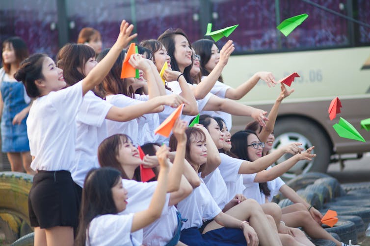 Vietnamese girls throw paper airplanes while celebrating their graduation.