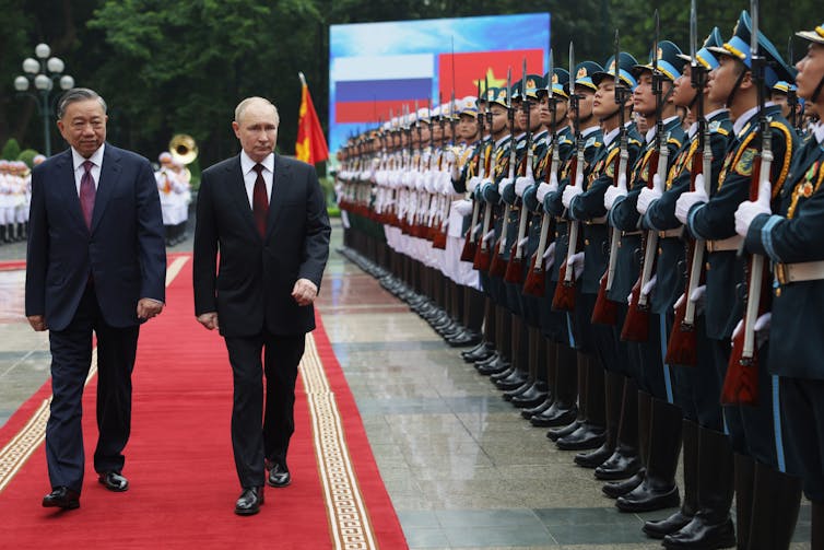 Putin walks along a red carpet next to a line of Vietnamese military personnel.