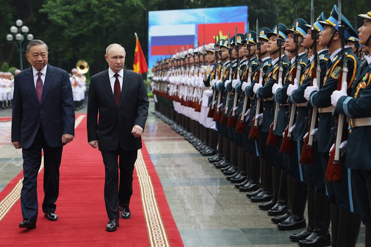 Putin walking down a red carpet next to a line of Vietnamese military personnel.