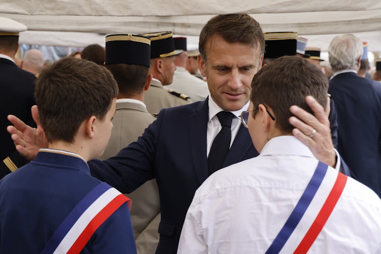 A dark-haired man embraces two young men, who are photographed from behind.