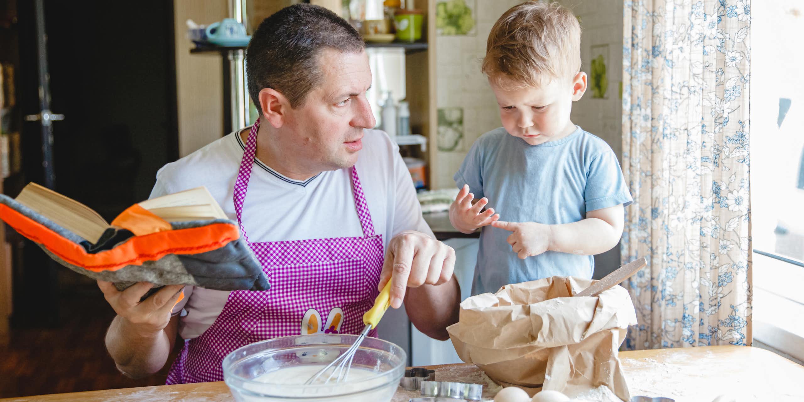 A father with a young son at the kitchen table at home preparing dough