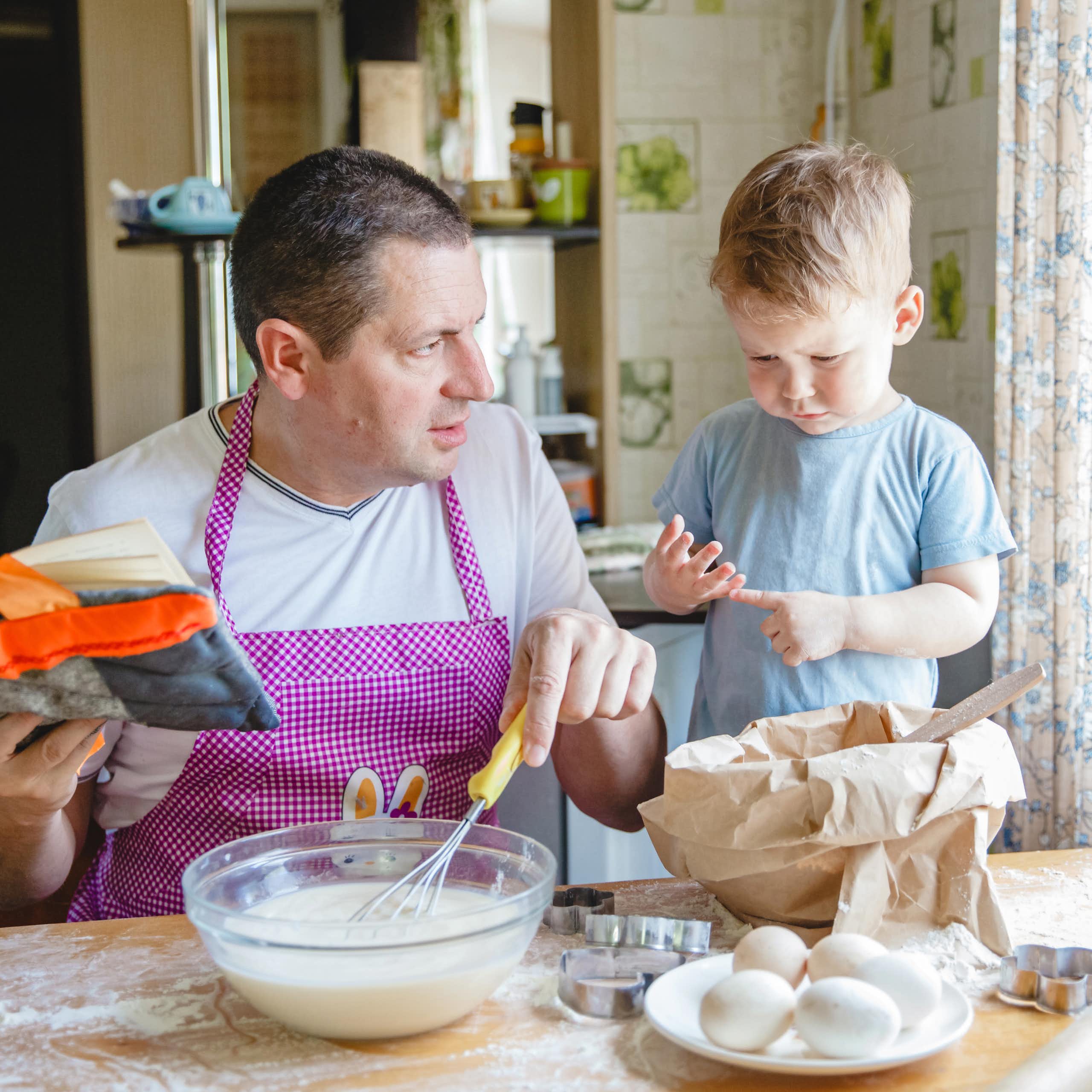 A father with a young son at the kitchen table at home preparing dough