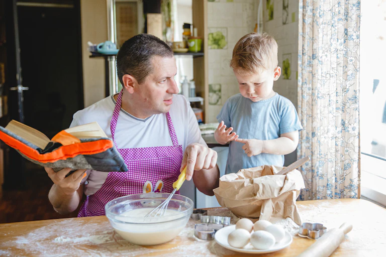 A father with a young son at the kitchen table at home preparing dough