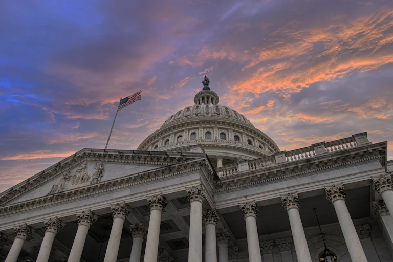 An imposing gray government building with a dome and an American flag flying from a pole.