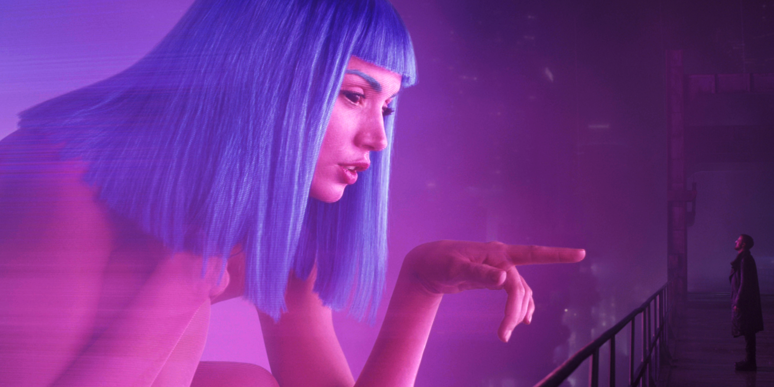 A massive holograph of a pink-skinned, blue-haired young woman points at a small man who gazes up at her.