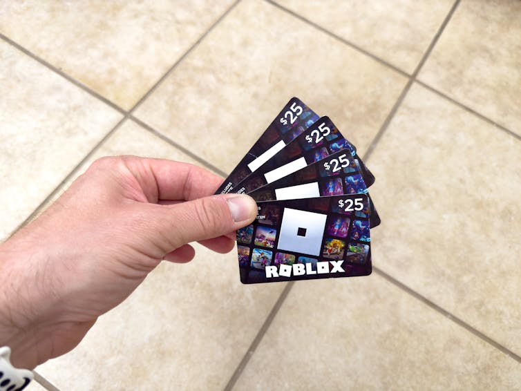 a hand holding four Roblox gift cards