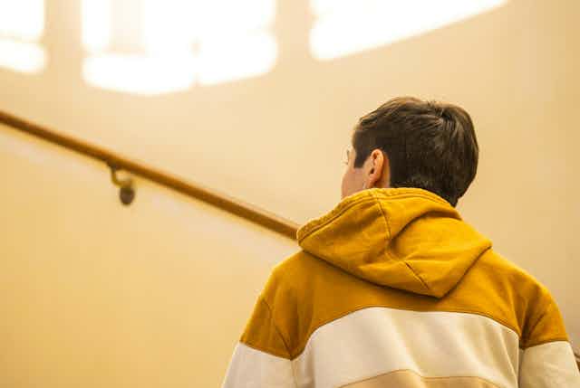 A young man in a hoodie jumper walks up a staircase.