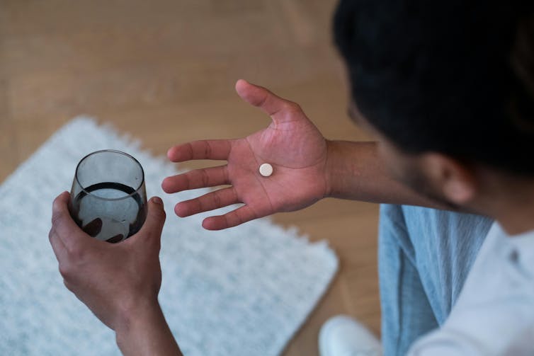The person is holding a pill and a glass.