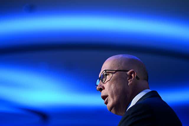 A man in glasses speaks in front of bright blue lights
