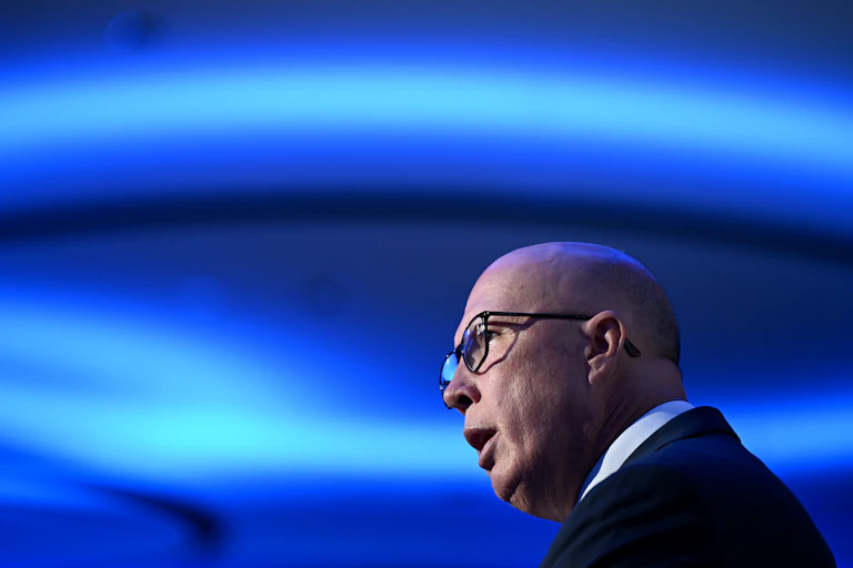 A man in glasses speaks in front of bright blue lights