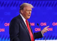 A white man makes a gesture with his hand during a presidential debate.