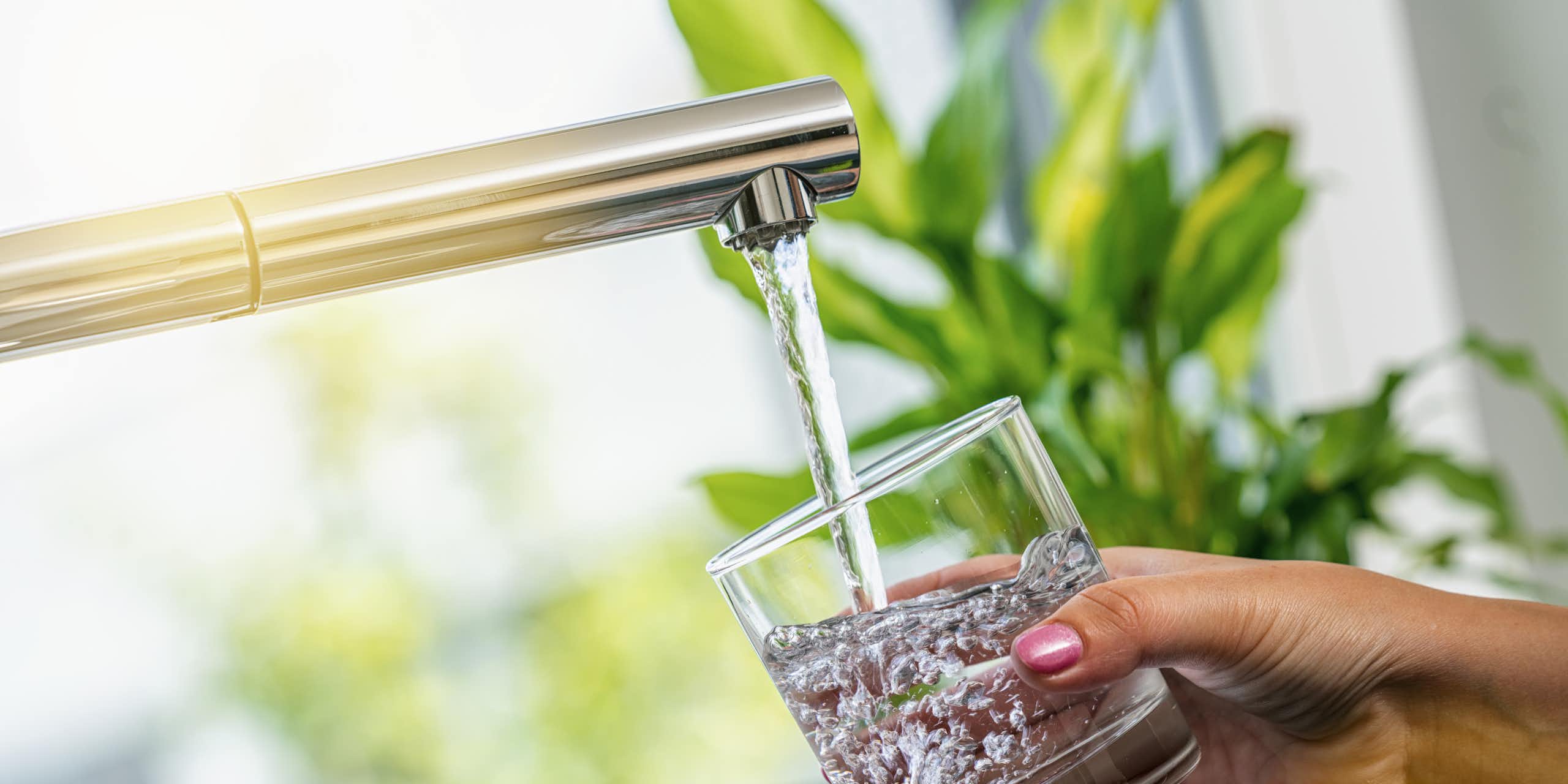 A woman's hand holds a glass of water being filled from a tap
