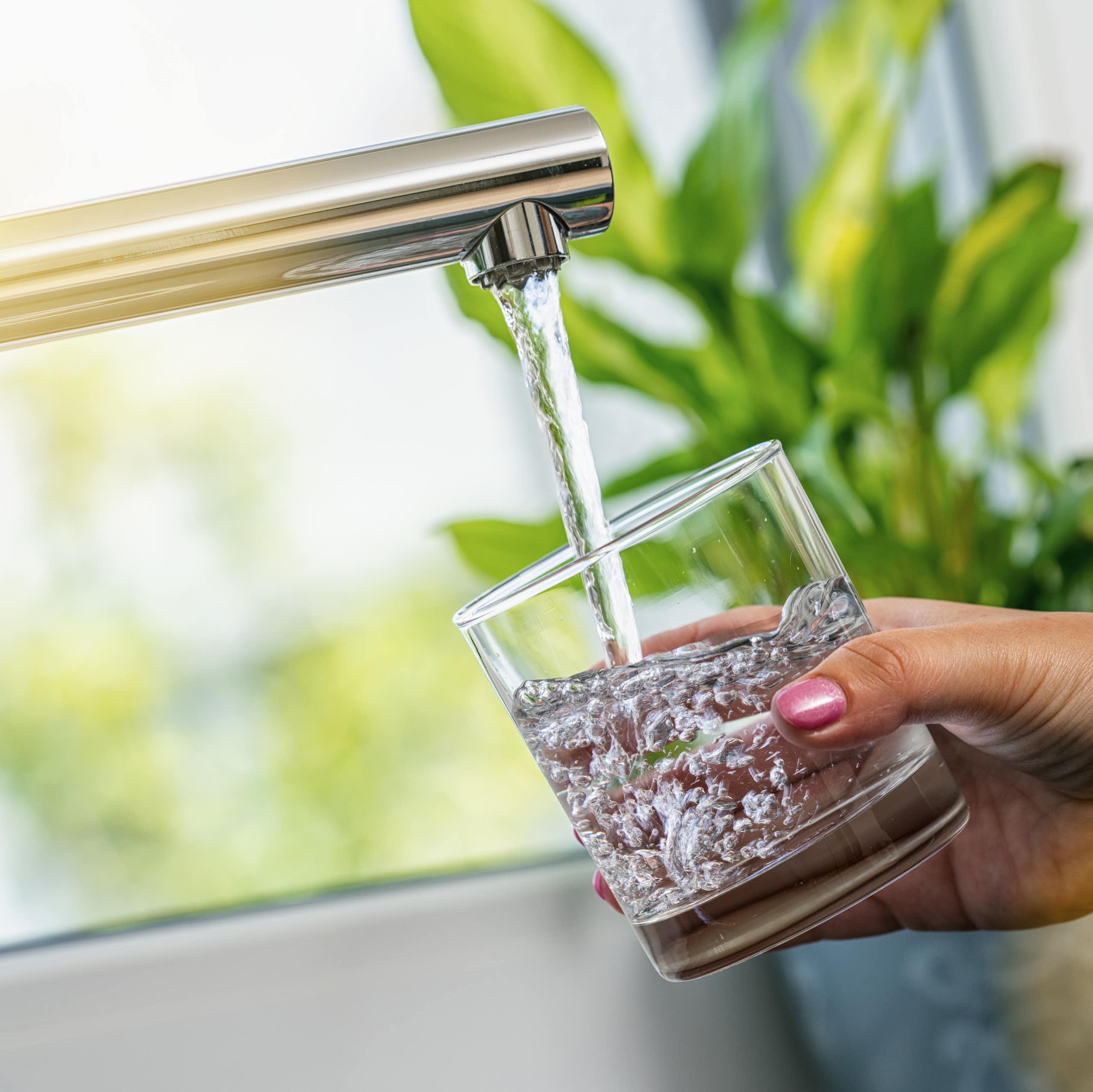 A woman's hand holds a glass of water being filled from a tap