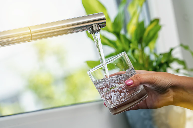 A woman's hand holds a glass of water being filled from a tap