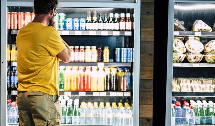 A man in a store looking at a fridge of drinks.