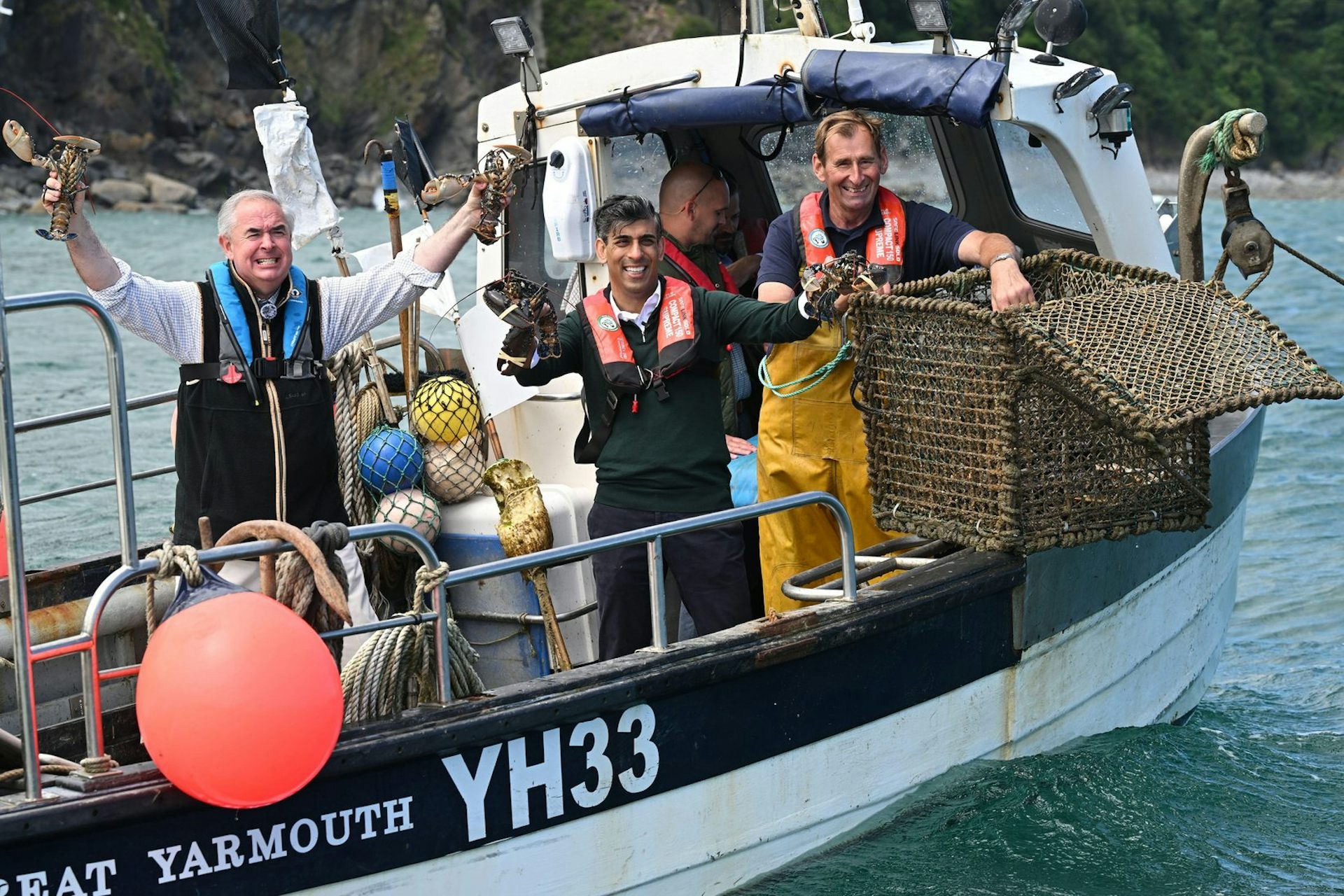 Rishi Sunak and Geoffrey Cox on a lobster boat in Devon, holding lobsters in their hands.