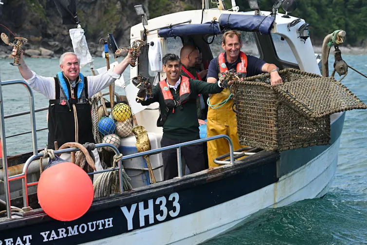 Rishi Sunak and Geoffrey Cox on a lobster boat in Devon, holding lobsters in their hands.