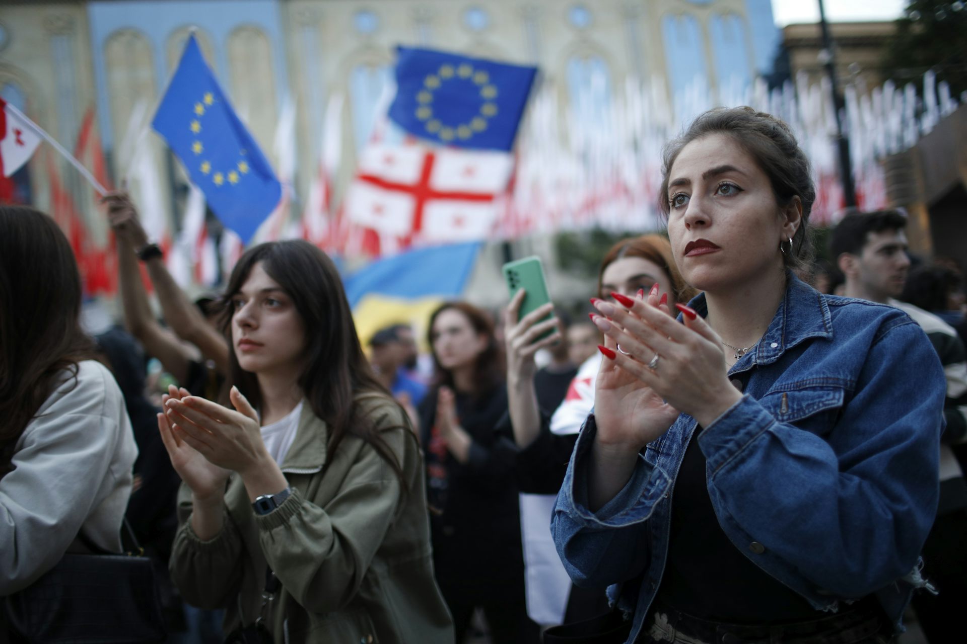 Women participating in a protest with Georgia and EU flags being waved in the background.