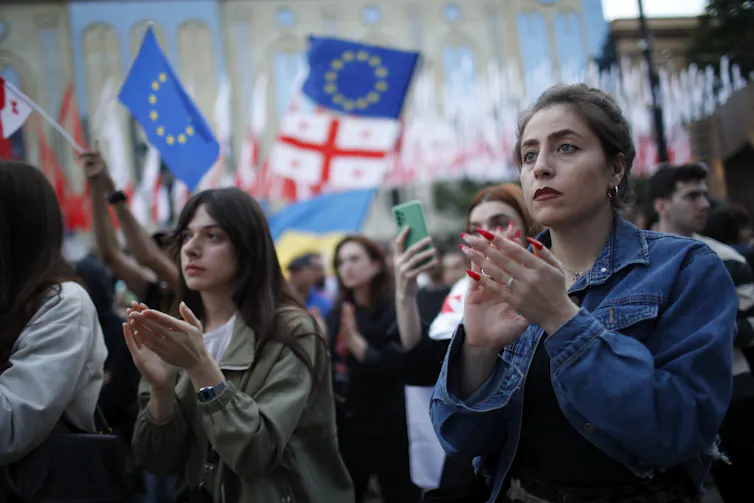 Women participating in a protest with Georgia and EU flags being waved in the background.