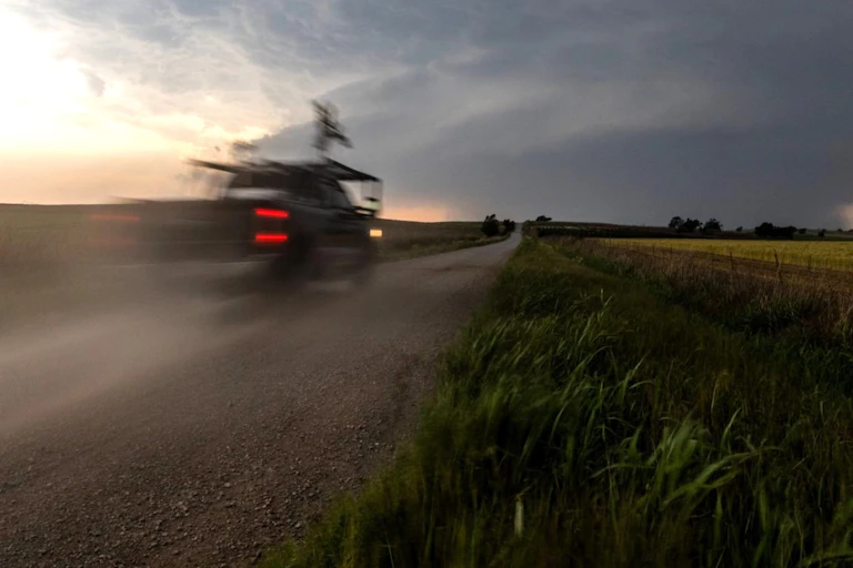 A pickup truck outfitted with instruments races down a gravel road toward a thunderstorm.