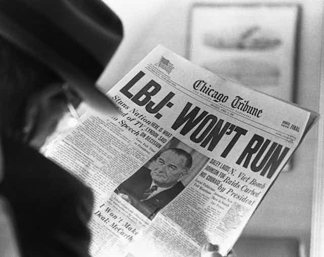A man is reading a newspaper headline that says LBJ won't run in very large letters.