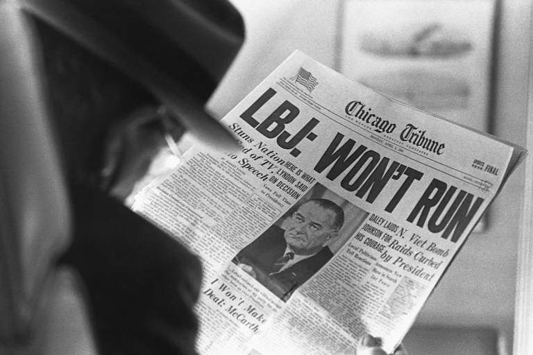 A man is reading a newspaper headline that says LBJ won't run in very large letters.