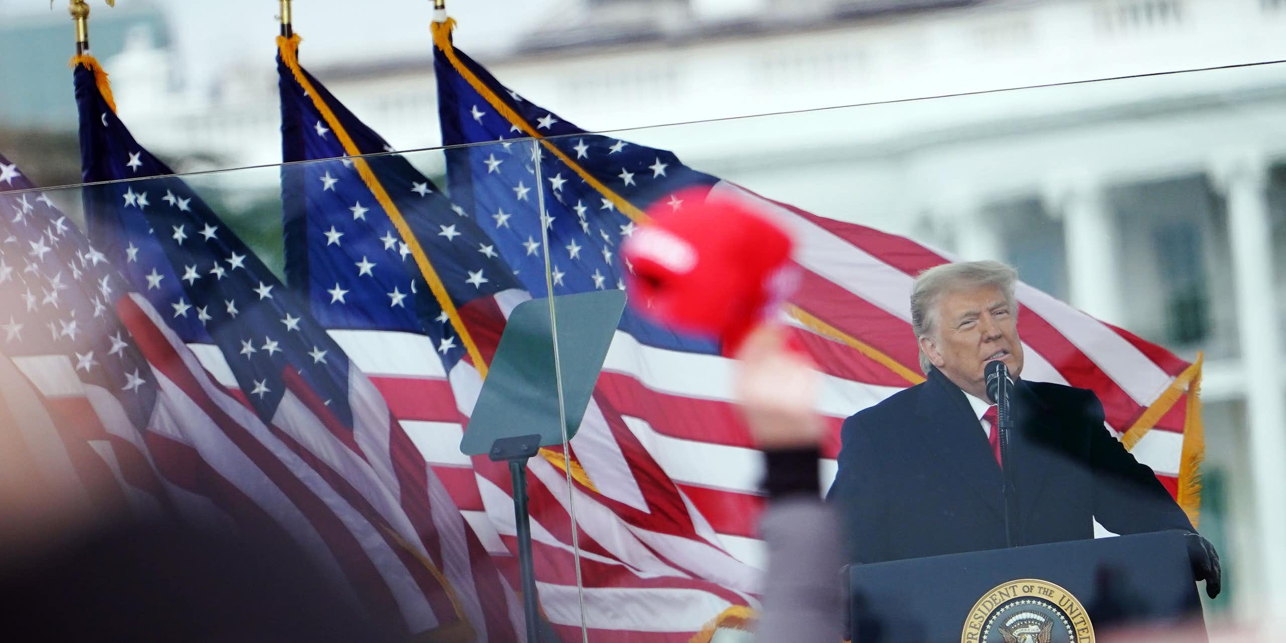 A man speaks in front of a row of American flags.