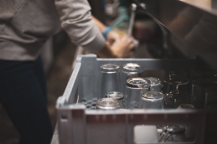 A person washing dishes in an industrial sink, visible from the shoulders down
