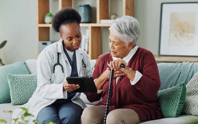 A health-care practitioner showing a tablet to a woman with gray hair holding a cane