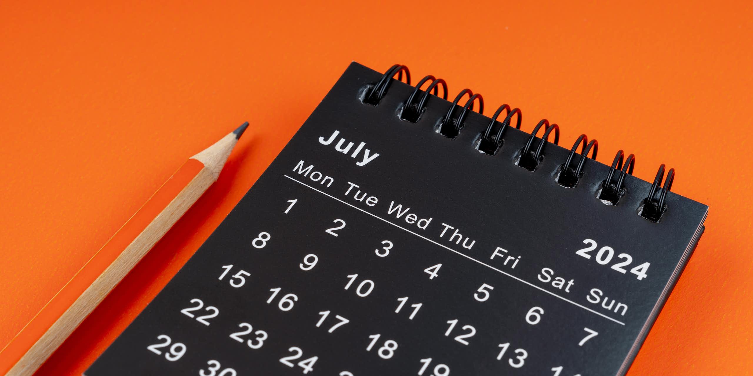Desk calendar seen on orange background with orange pencil 